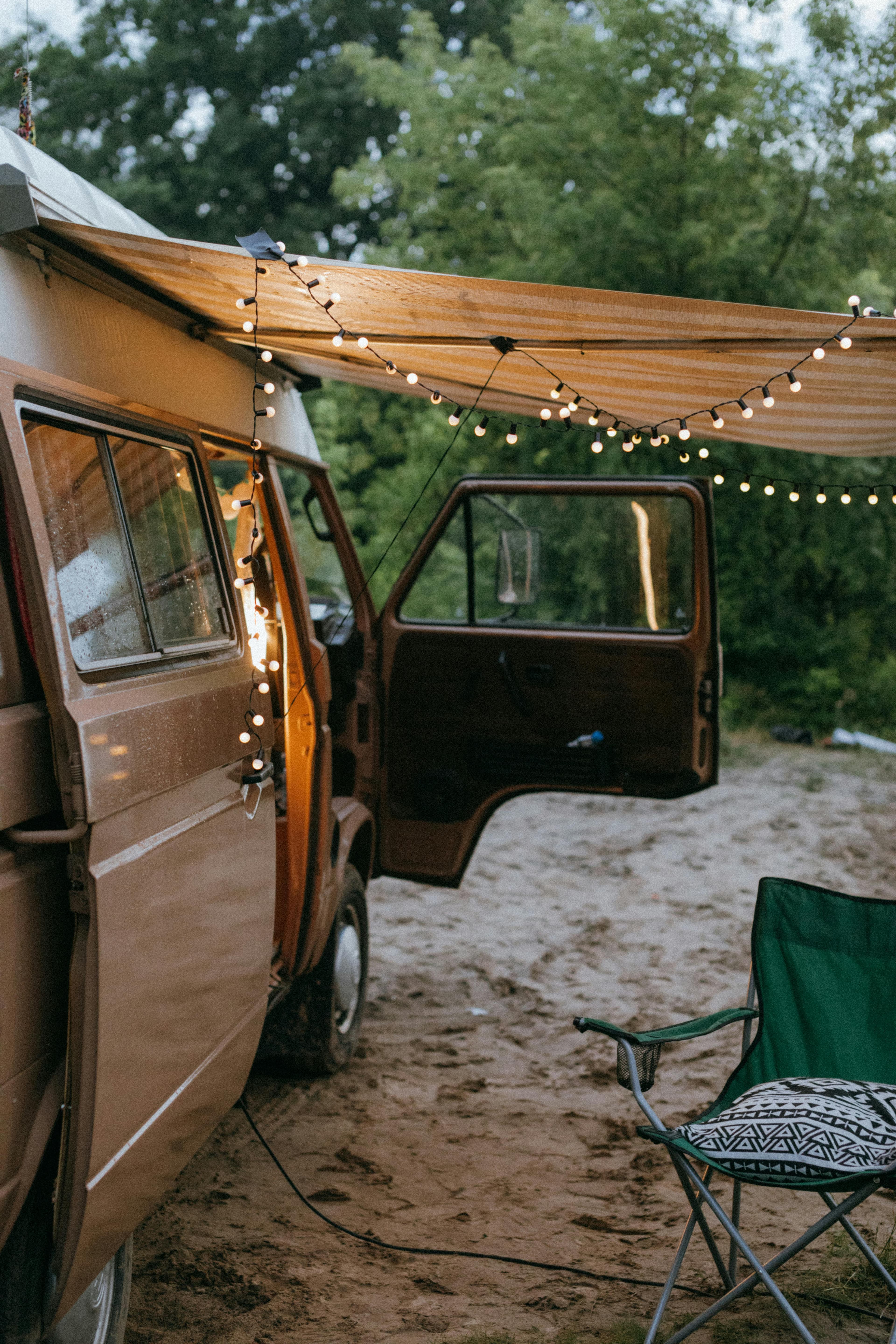 Campervan at dusk with warm interior lights and string lights under the awning